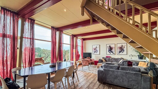Un vaste espace de vie doté d’un plancher en bois, d’une table à manger avec des chaises, d’un canapé et d’un escalier.