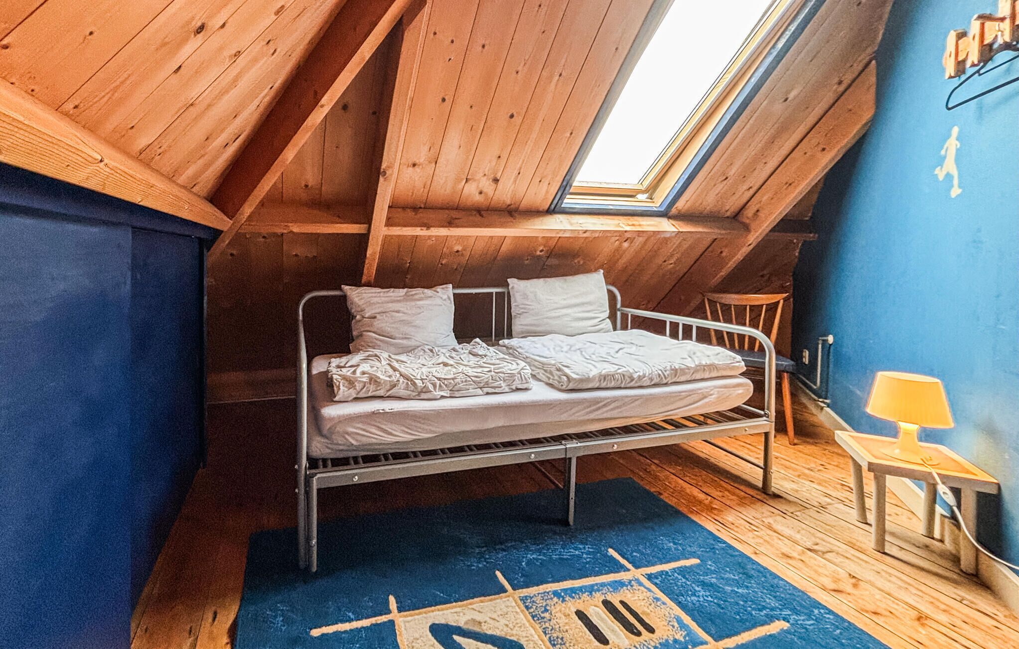 Une chambre de style « loft », dotée d’une lucarne, d’un cadre de lit en métal et d’un mur d’accent bleu.
