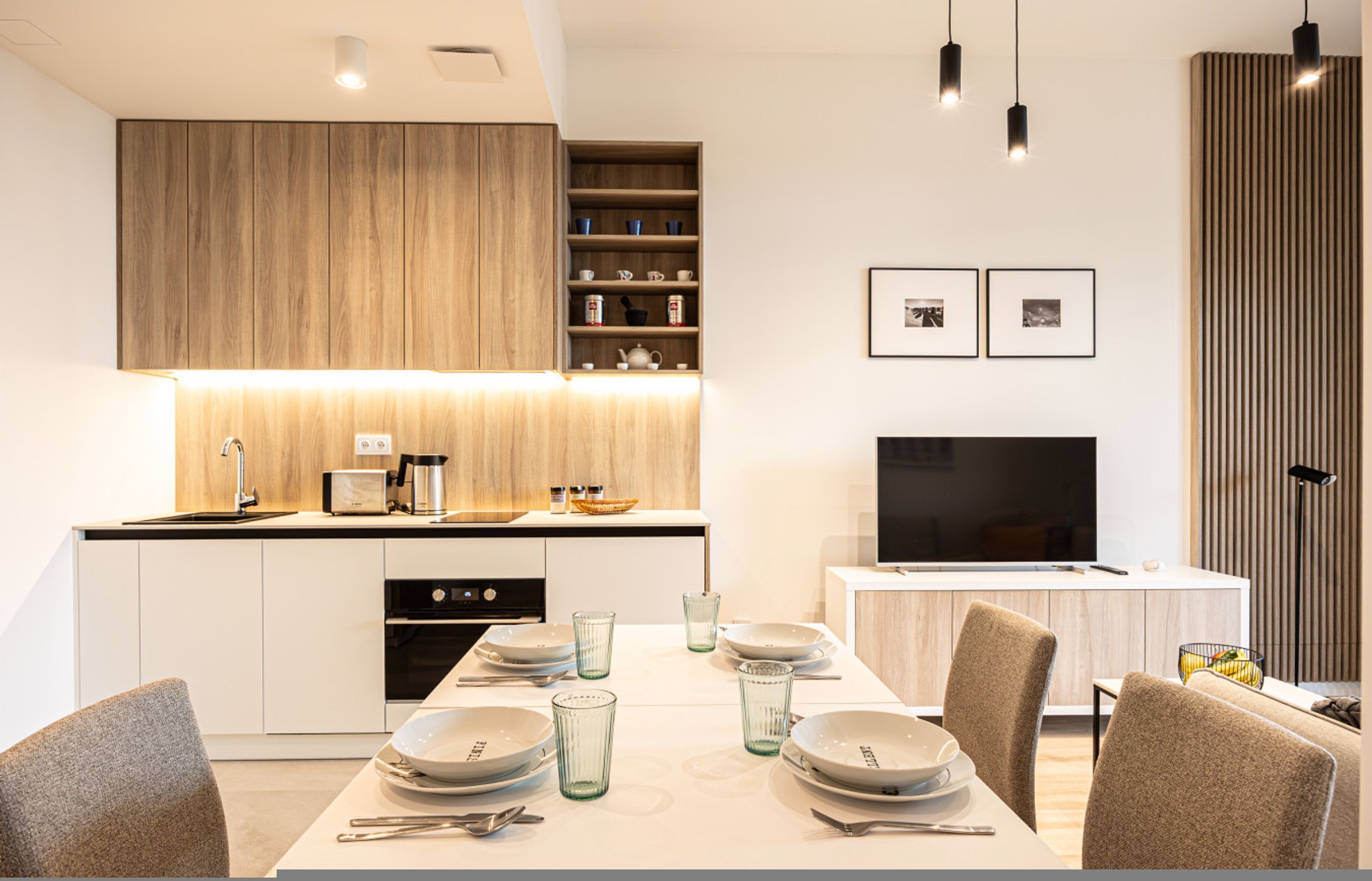 Una cocina moderna con comedor, armarios de madera, un televisor y una mesa de comedor para cuatro personas.