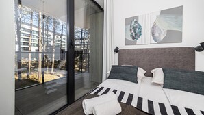 Een moderne hotelkamer met een grote schuifglazen deur, een bed met gestreepte beddengoed en twee abstracte kunstwerken aan de muur.