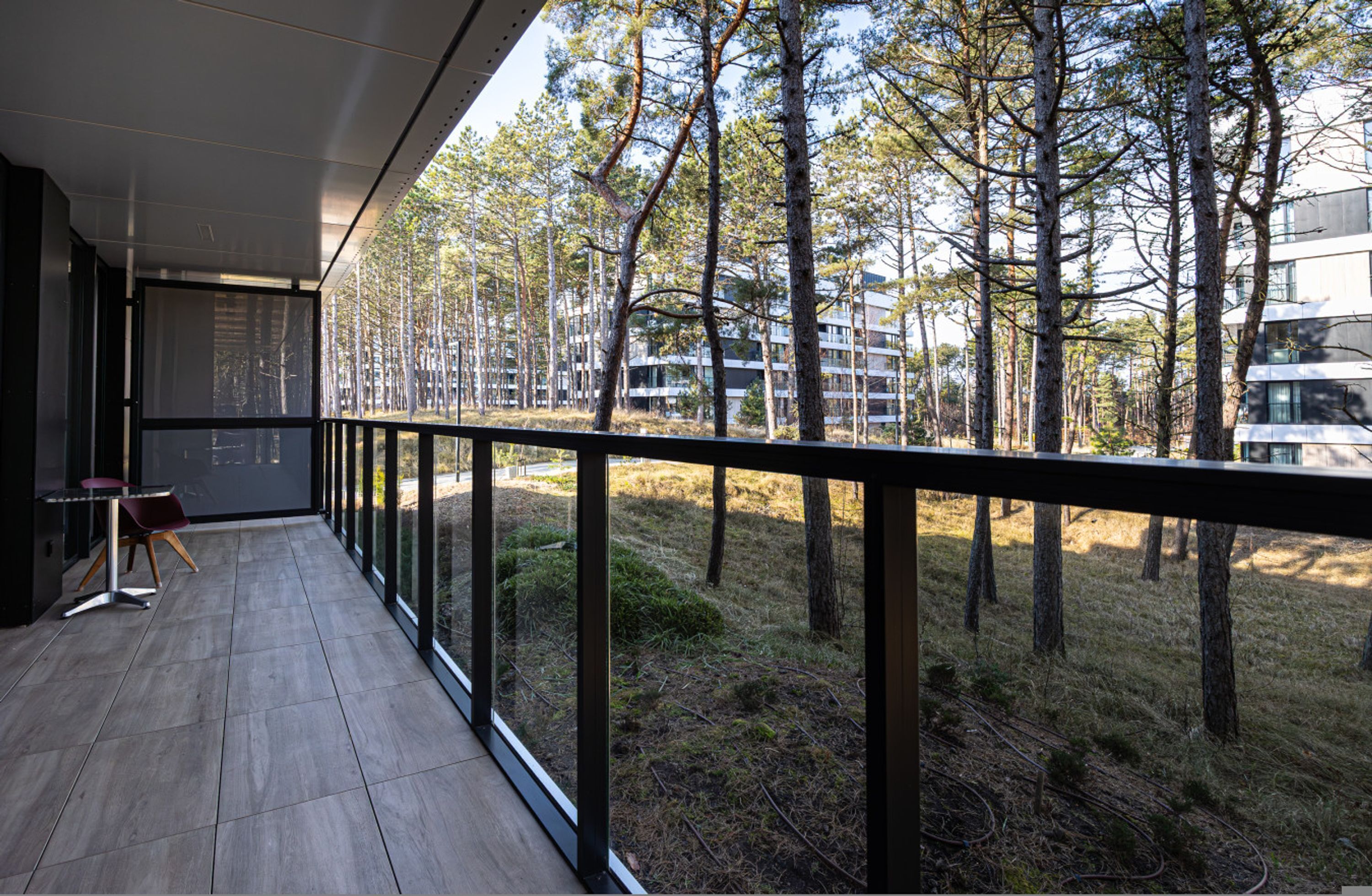 A modern balcony with a view of a forest and buildings.