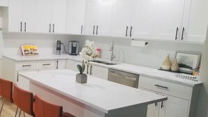 Una cocina moderna con armarios blancos, una isla central y un comedor con sillas rojas.