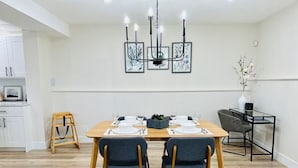 Un comedor con una mesa de madera, dos sillas, una araña y obras de arte enmarcadas en la pared.