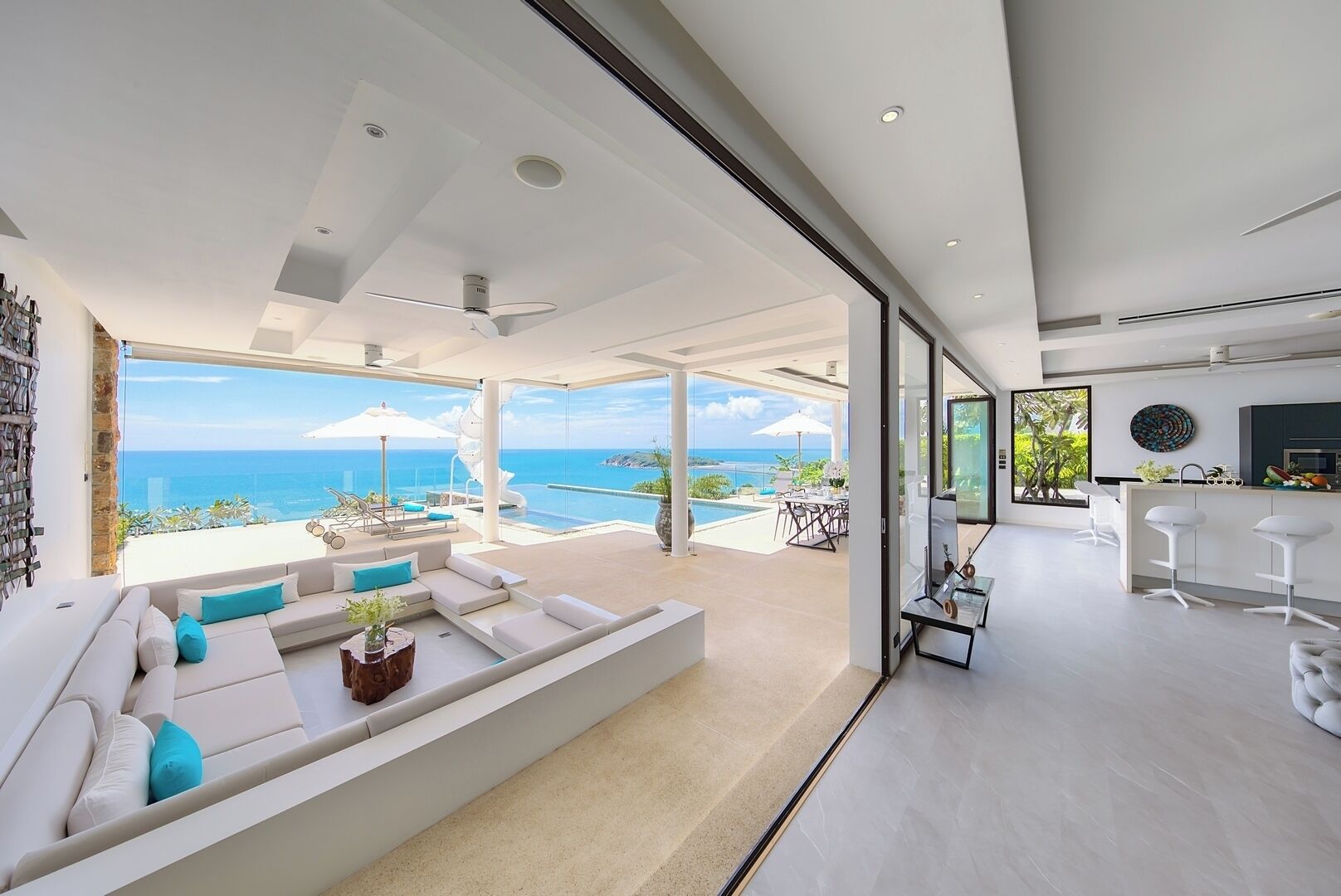 Uma sala de estar moderna com um sofá branco grande, uma área de jantar com balcão e vista para o oceano.