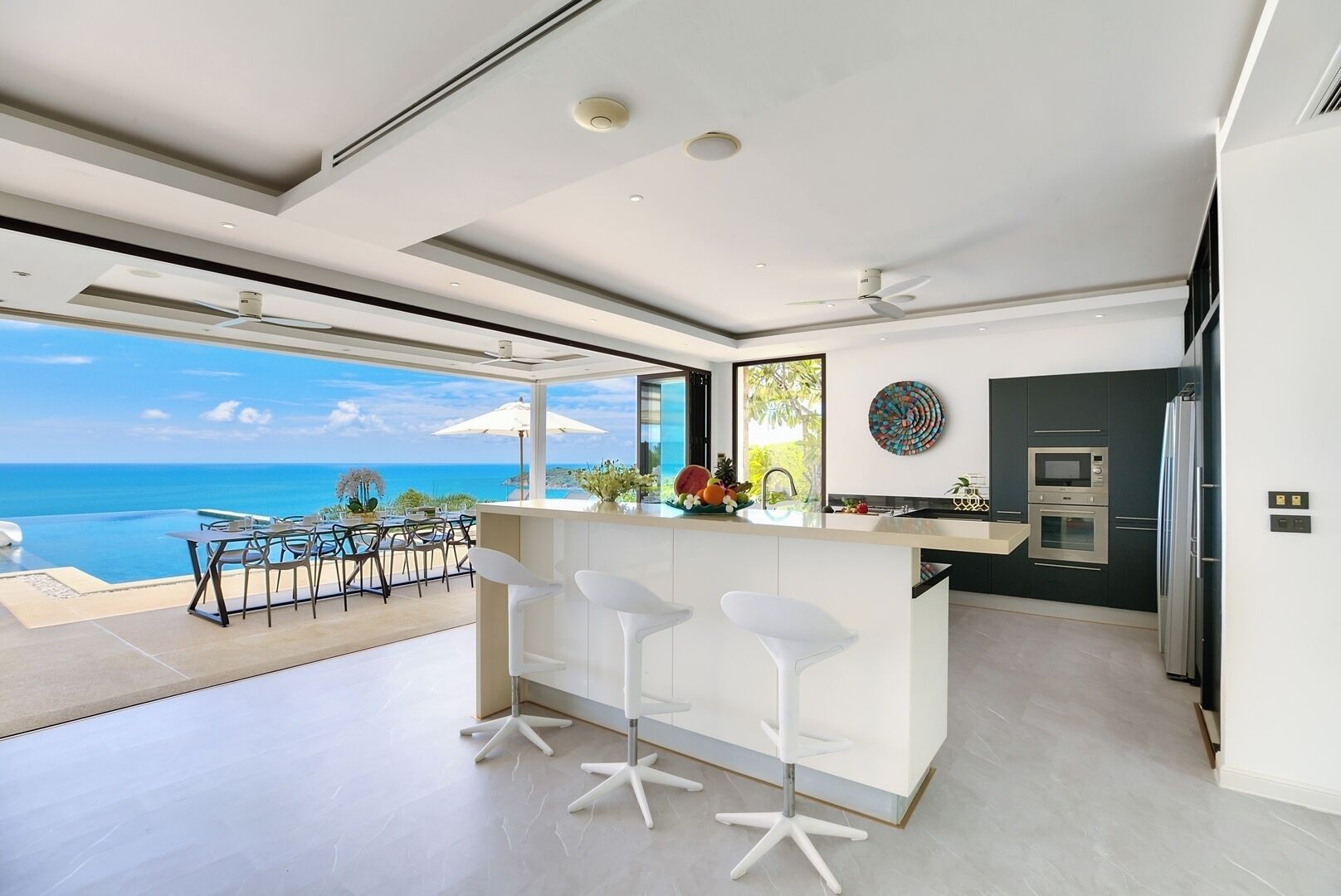 Uma cozinha moderna com vista para o oceano, uma área de refeições com cadeiras e um balcão.