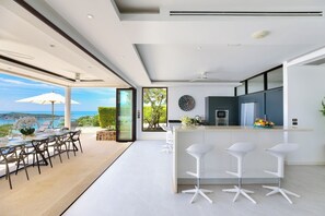 A modern kitchen with a bar area, large windows, and a view of the ocean.