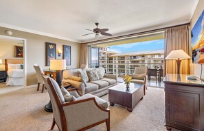 Ein Hotelzimmer mit Balkon, einer Couch, einem Couchtisch, einem Fernseher und Kunstwerken an den Wänden.