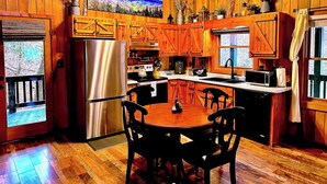Interior de una cabaña de madera con cocina, comedor y un amplio ventanal.