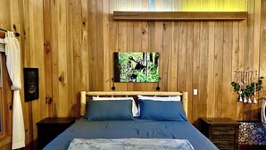 Una habitación con paneles de madera, una cama, un cuadro en la pared y un pequeño armario de madera.