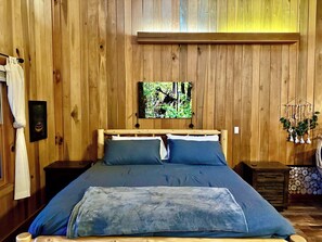 A wooden-paneled room with a bed, a painting on the wall, and a small wooden cabinet. - Cozy Studio Smoky Mountain Cabin - Unbeatable Location (Pigeon Forge)