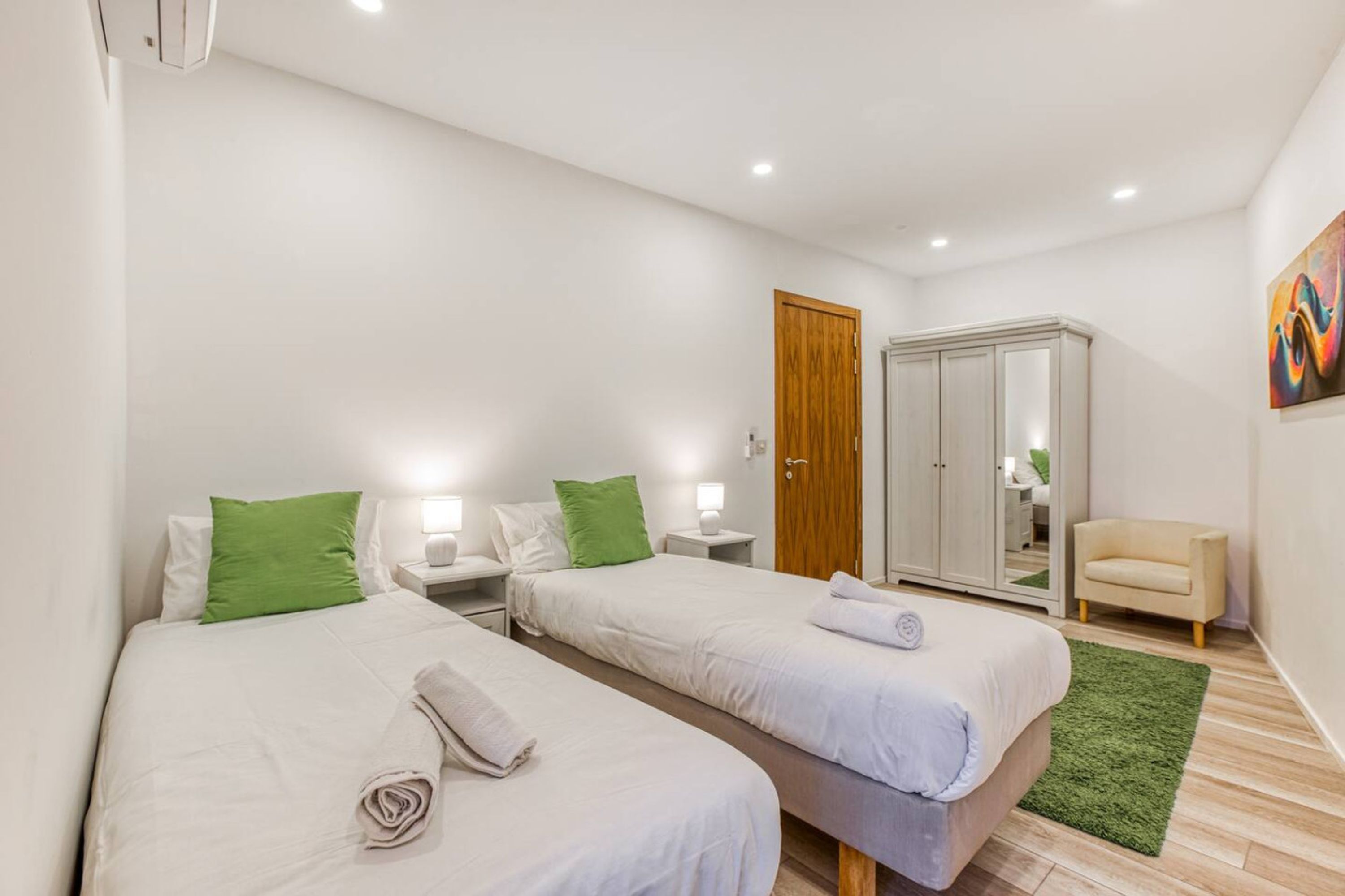 Una habitació d'hotel amb dos llits, un armari, una cadira i un quadre a la paret.