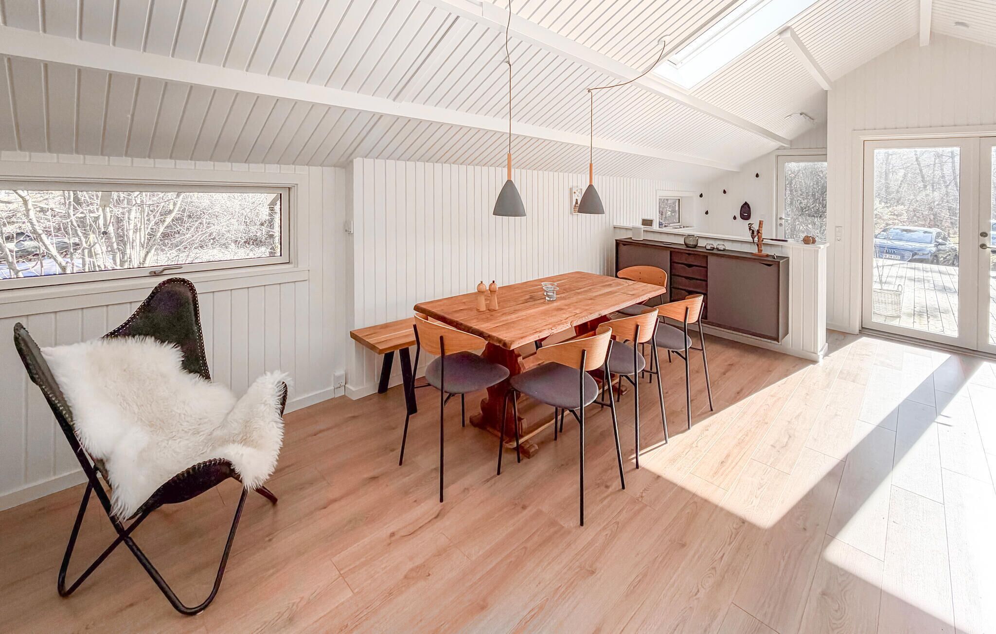 A modern kitchen with a wooden table and chairs, a white interior, and a view through the window.