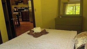 A bedroom with a bed, a bedside table, a mirror, and a window with a view of greenery. - 1A Jungle Mountain Getaway (Ciudad Cortés)