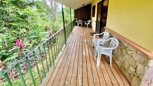 A wooden deck with white plastic chairs, a stone wall, and a yellow building. - 1A Jungle Mountain Getaway (Ciudad Cortés)