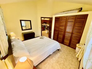 Une chambre d’hôtel équipée d’un lit, d’un bureau, d’un miroir, d’une armoire et d’une salle de bain visible à travers une porte ouverte.