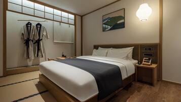 Habitación de hotel con cama, mesitas de noche, una mesita con lámpara, un cuadro en la pared y ventana con vistas.