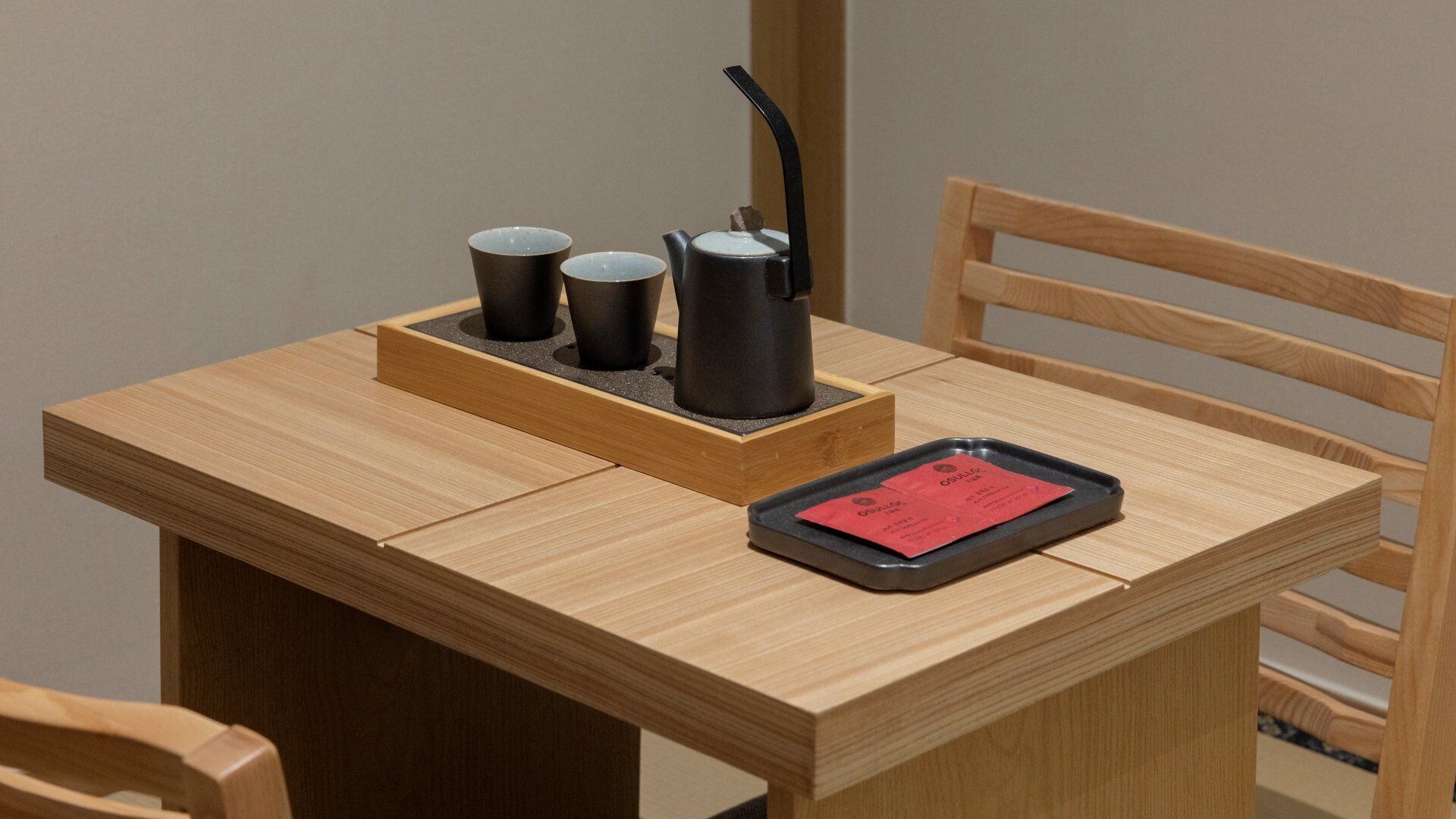 Una mesa de madera con una bandeja que contiene dos tazas y una tetera, y una tableta que muestra un menú rojo.