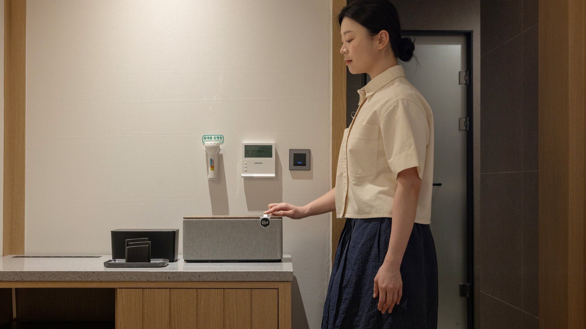 A person interacting with a Samsung device on a counter, with a small black object and a grey box nearby.