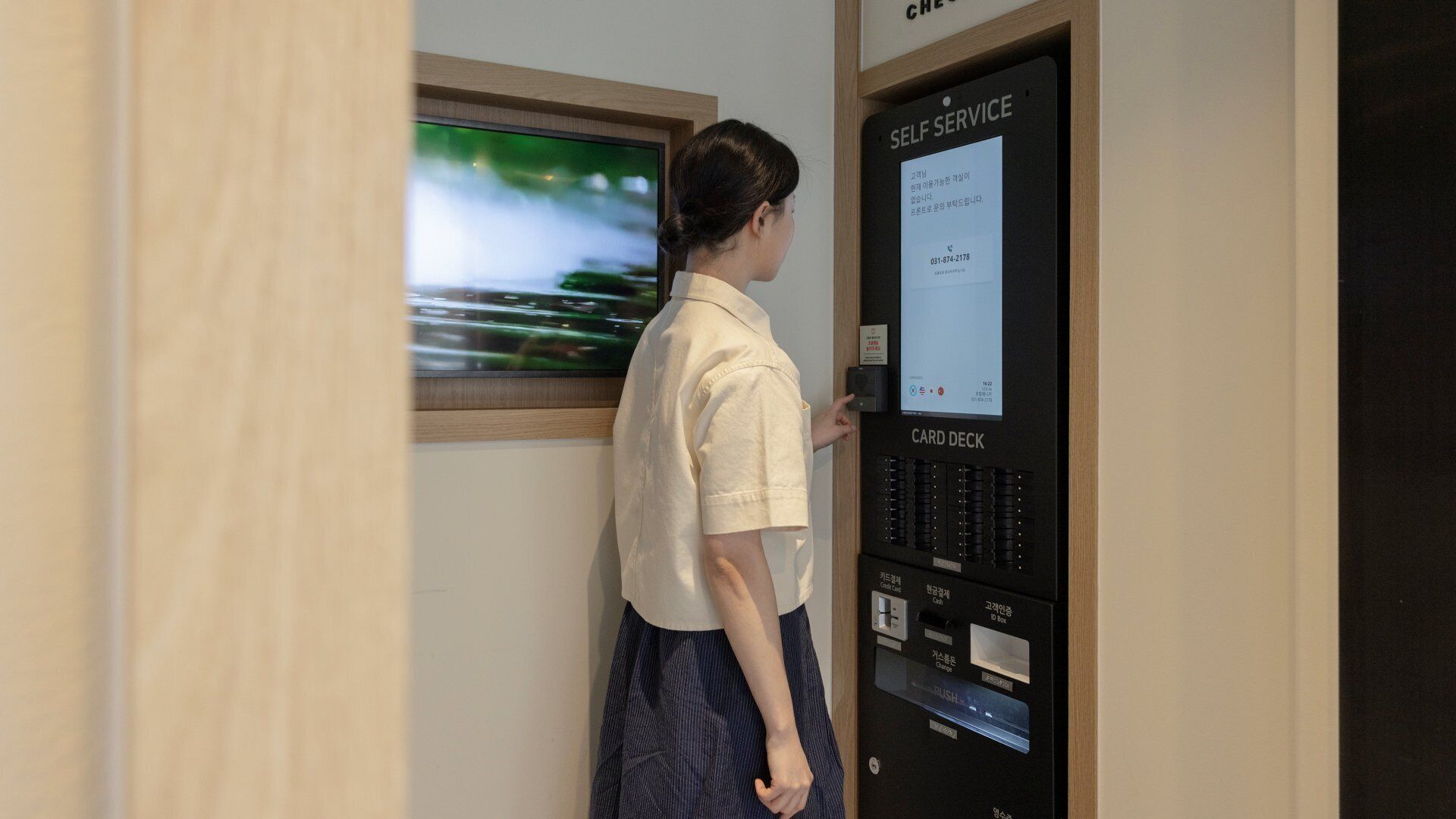 Una persona utilizza un distributore automatico di carte in una stanza con una porta in legno e una finestra che mostra un paesaggio verde.