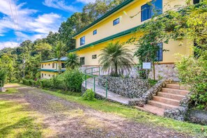 A yellow building with a stone staircase and a green railing, surrounded by lush greenery. - Villa 30B Toucan Valley Jungle Resort (Ciudad Cortés)