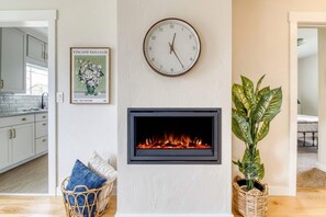 Un salón con chimenea, un reloj, un cuadro enmarcado y una planta en maceta.