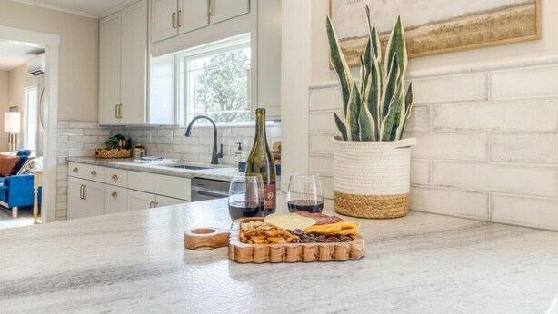 A kitchen with white cabinets, a marble countertop, a wine bottle, glasses, and a plant. - Downtown Redmond 4BR Walk to Food & Brews (Redmond)