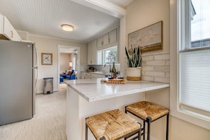 Una cocina con una isla central, taburetes de bar, un refrigerador y una planta en maceta.
