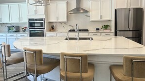 A modern kitchen with white cabinets, a large island with bar stools, stainless steel appliances, and pendant lighting. - Luxury Modern Retreat with Pool & Spa – Near the Strip (Las Vegas)