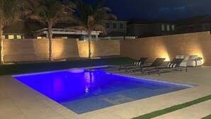 A swimming pool with a blue light, lounge chairs, and a brick wall. - Luxury Modern Retreat with Pool & Spa – Near the Strip (Las Vegas)