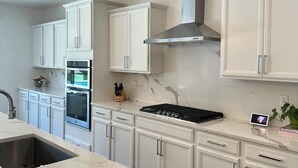 A modern kitchen with white cabinetry, a stainless steel range hood, a built-in oven, and a marble countertop. - Luxury Modern Retreat with Pool & Spa – Near the Strip (Las Vegas)