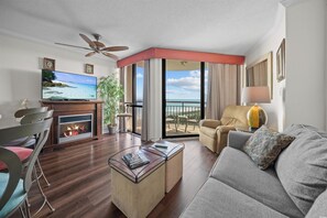 A living room with a flat-screen TV, a fireplace, a sofa, a coffee table, and a balcony with a view. - Myrtle Beach Oceanfront Escape w/Private Balcony - Stunning Beach & City Views (Myrtle Beach)