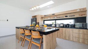 A modern kitchen with a central island, wooden chairs, and a black countertop. - Villa Cansavina (Seminyak)
