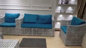 Un salon moderne avec des meubles en osier, un canapé gris agrémenté de coussins bleus et une étagère murale décorative.