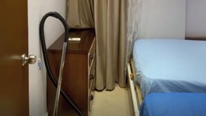 Une petite pièce comprenant un lit, un bureau, un appareil de climatisation et un rideau.