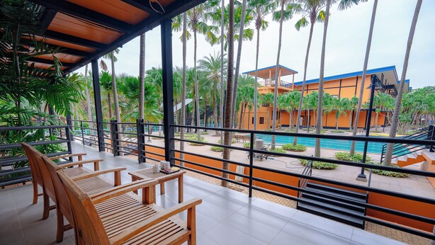 Un área de estar al aire libre con techo, con bancos de madera, con vista a una piscina y un edificio de paredes naranja y techo azul.