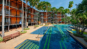Un hotel con piscina, palmeras y un edificio de varios pisos con balcones.