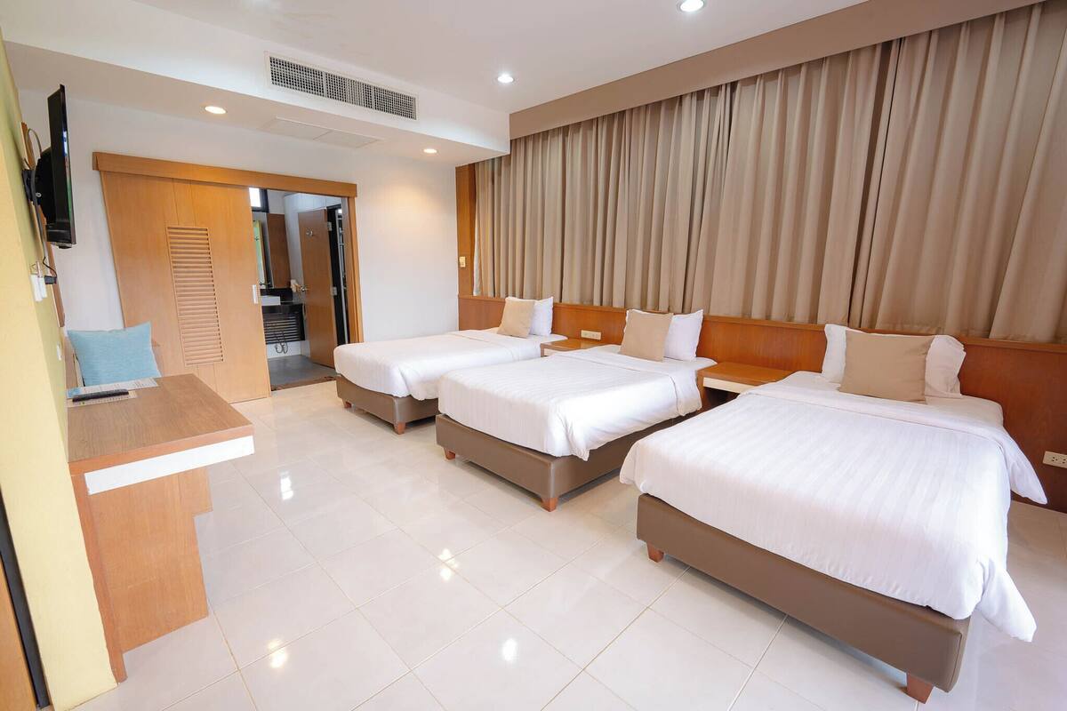 A hotel room with three beds, a desk, and a TV.