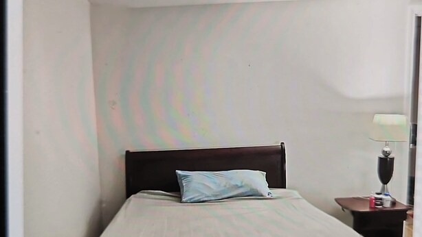 A single bed with a wooden headboard, a bedside table with a lamp, and a plain wall. - Cozy 1-bedroom studio in quaint Belleville with AC and gym access (Belleville)