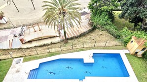 Ein Pool im Freien mit freiem Blick auf die Umgebung, darunter eine Palme, eine umzäunte Terrasse und ein kleines Gebäude.