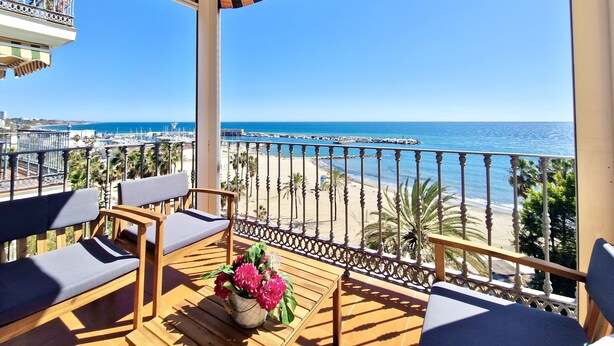 Ein Balkon mit Blick auf Strand und Meer, Holzmöbel und ein Blumentopf.