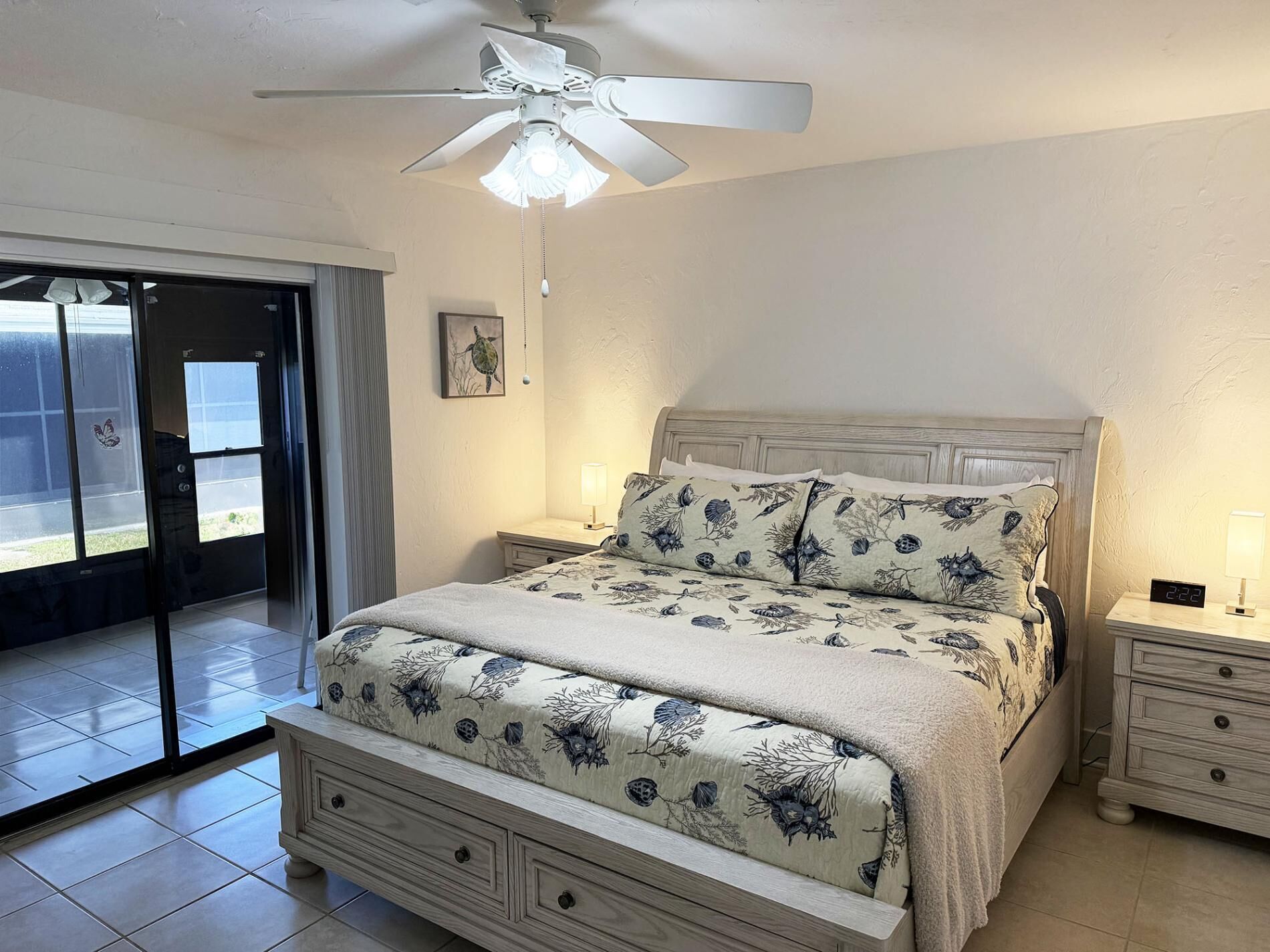 A bedroom with a bed, a nightstand, a ceiling fan, a window, and a door.