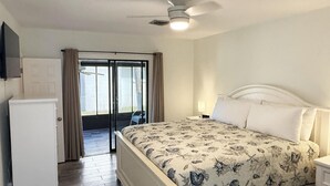 Une chambre à coucher comprenant un lit, une table de chevet, un ventilateur de plafond et une porte-fenêtre coulissante donnant sur un espace extérieur.