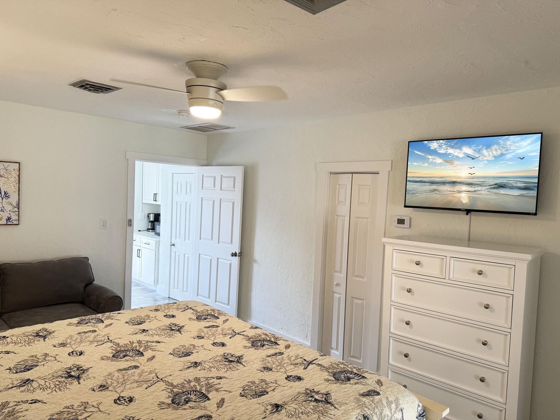 A bedroom with a bed, a ceiling fan, a dresser, and a TV on the wall.