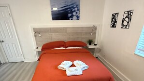 Ein Schlafzimmer mit Bett, Kopfstütze, Wandkunst, einem gemusterten Teppich und einer Tür.