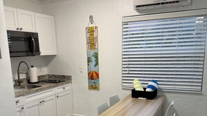 Eine moderne Küche mit weißen Schränken, einer Mikrowelle und einem Essbereich mit Holztisch und weißen Stühlen.