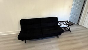 Ein Zimmer mit einer schwarzen Couch, einem kleinen Holztisch und einem gemusterten Teppich.