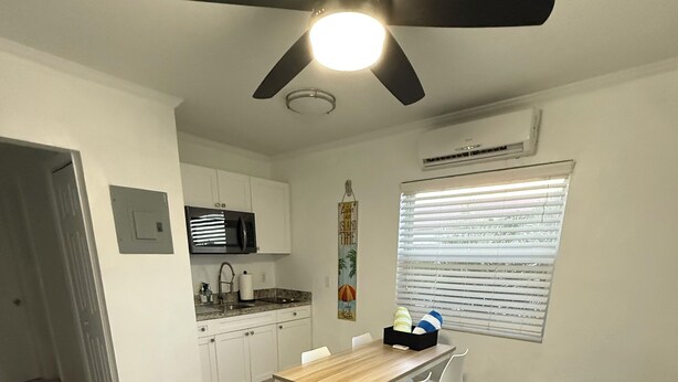 Ein kompakter Wohnraum mit Essbereich, Küchenzeile, Deckenventilator und einem schwarzen Sofa.