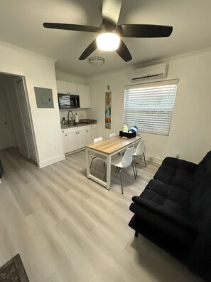 A compact living space with a dining area, kitchenette, ceiling fan, and a black sofa. - 116 YARDS FROM THE BEACH (Deerfield Beach)