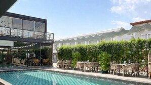 Une piscine entourée de verdure et de bâtiments, avec des chaises longues et un espace bar.