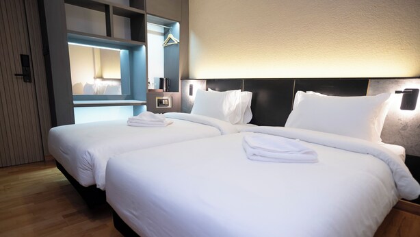 Une chambre d’hôtel avec deux lits, un miroir, une table de chevet et un porte-manteau mural.